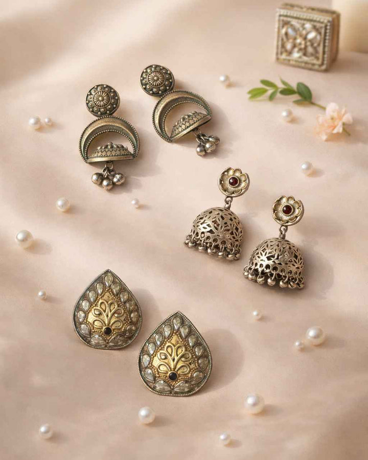 Ornate earrings on a soft beige background with pearls and a candle.