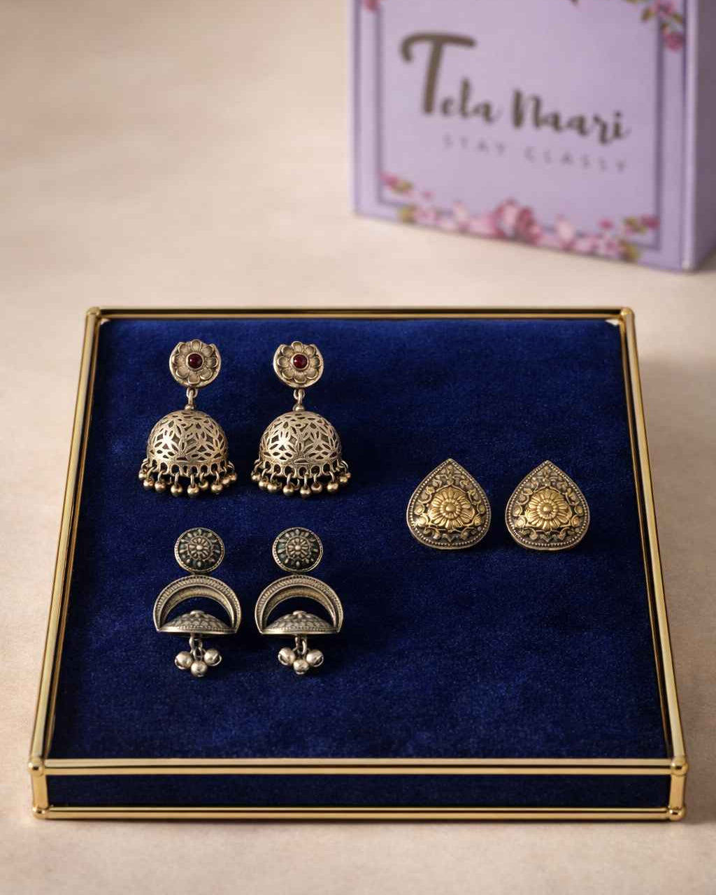 Set of gold earrings on a blue cushion with a Tela Naari box in the background