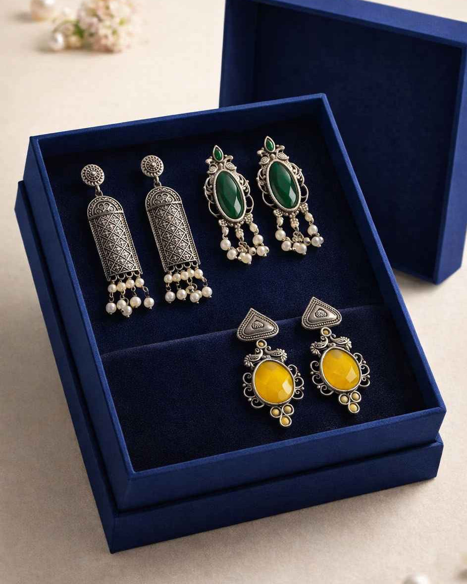 Set of silver earrings with green and yellow stones in a blue jewelry box.