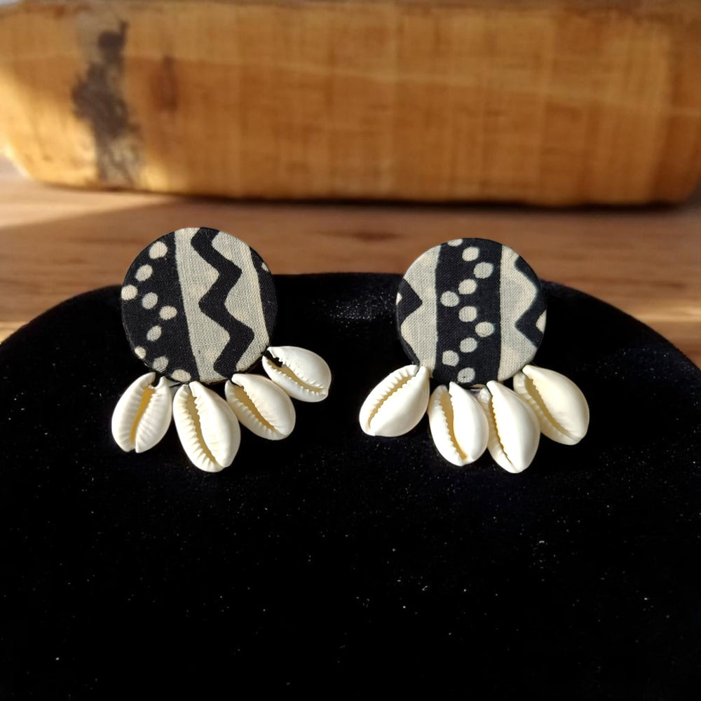 Pair of earrings with black and white patterned tops and cowrie shell-like bottoms on a black cushion.