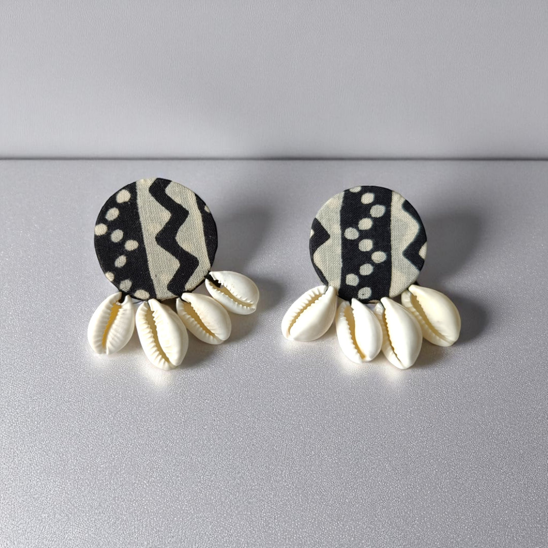 Pair of earrings with black and white patterned tops and cowrie shell bases on a gray background
