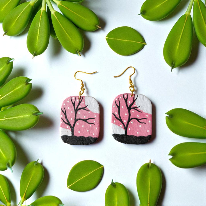 Pair of earrings with tree design on a white background with green leaves.