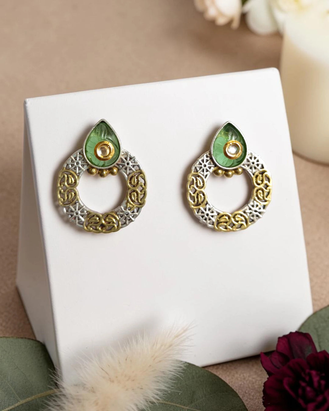 Pair of ornate earrings with green and gold design on a white stand.