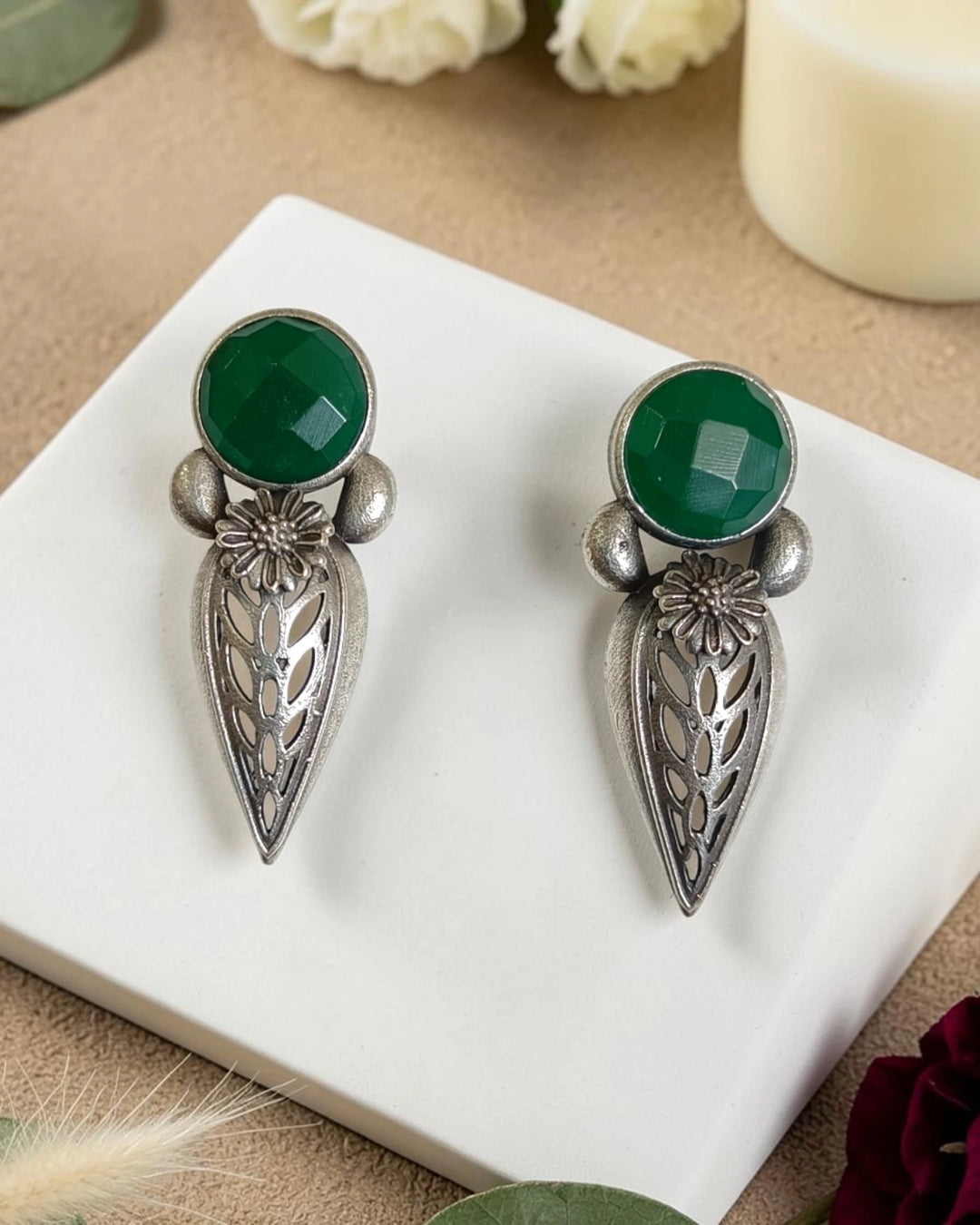 Luminous emerald green stones shape the centre of this teardrop stud.
