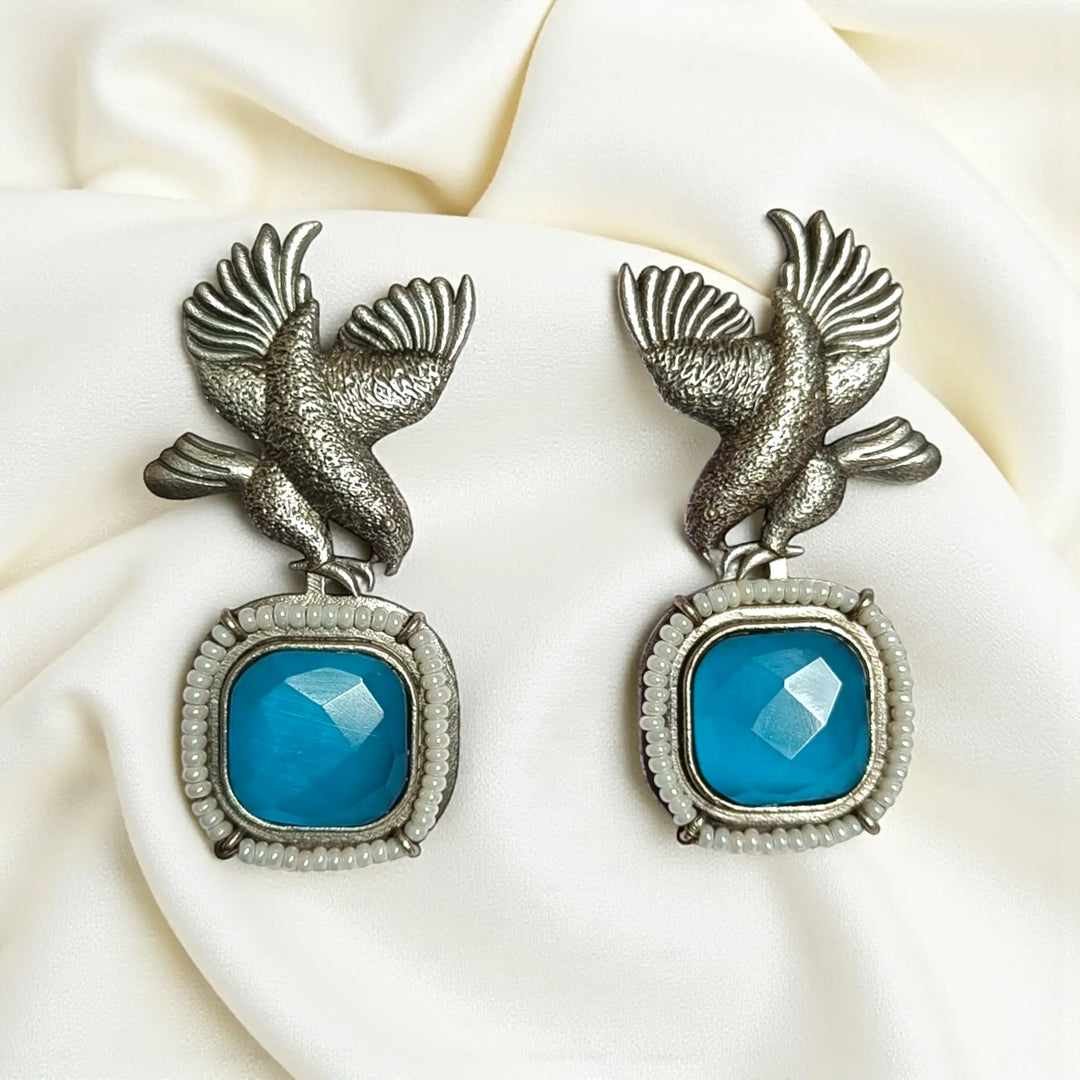 Delicate avian silhouette pairs brass with silver-plated stone detailing.