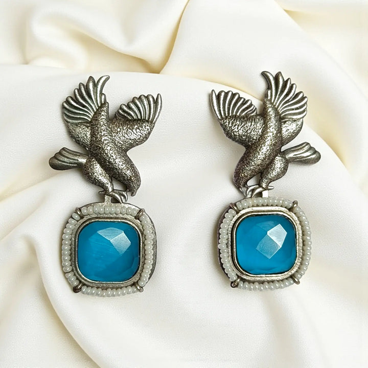 Delicate avian silhouette pairs brass with silver-plated stone detailing.