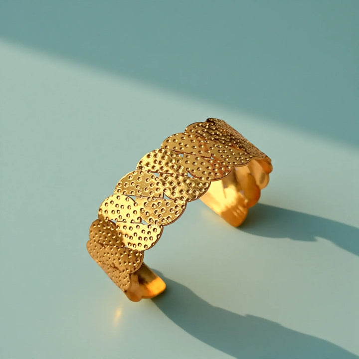 Polished gold surface highlights the scalloped texture of this cuff.
