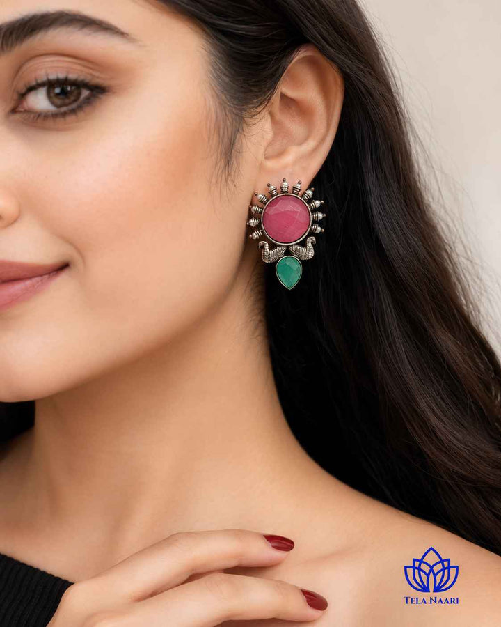 Pink gemstone accents sit within the oxidised silver-plated frame.